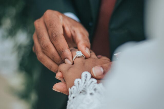 man putting wedding ring on woman's finger
