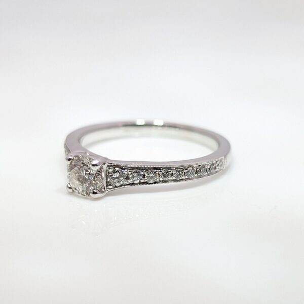 This 18ct white gold diamond engagement ring has an elegant milgrain edge encasing the shoulder stones, and a high-set centre stone making it ideal for your future wedding band.
