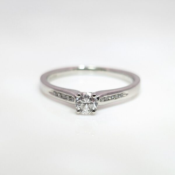 A classic four claw 0.30ct solitaire diamond engagement ring with diamond set shoulders, in a sleek platinum band.