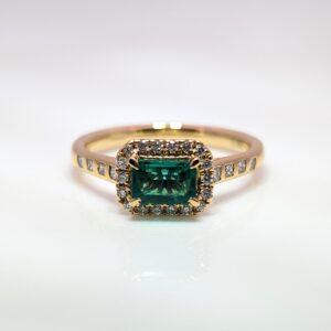 Discover our Diamond And Emerald Cluster Ring With Diamond Shoulders in 18ct Yellow Gold. Emerald jewellery is a timeless gift, but is especially meaningful to those with a May birthday.